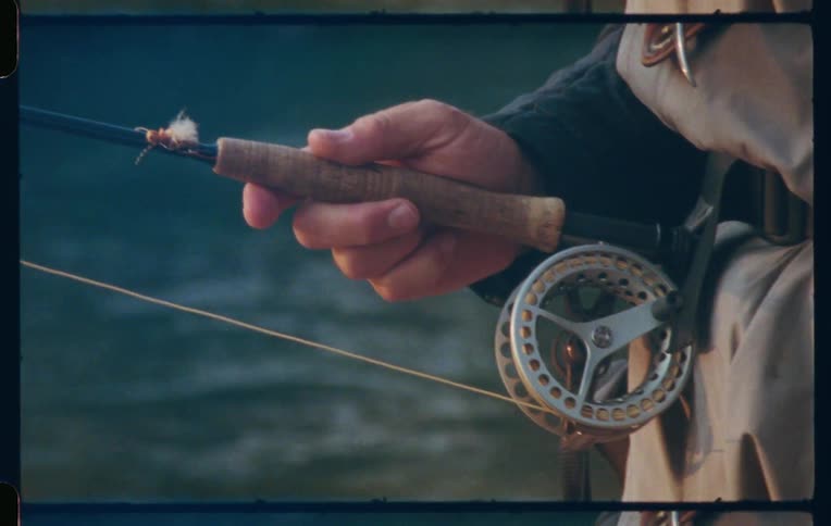 Tight shot of a fishing rod and reel prepared with a fly lure by the water