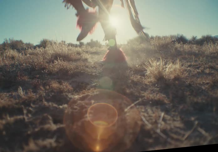 Male dancer wearing native american attire kicks up dust while dancing in a field on a sunny day