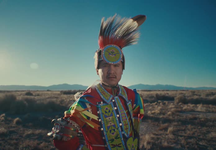 A dancer in vibrant traditional attire standing confidently in a desert landscape