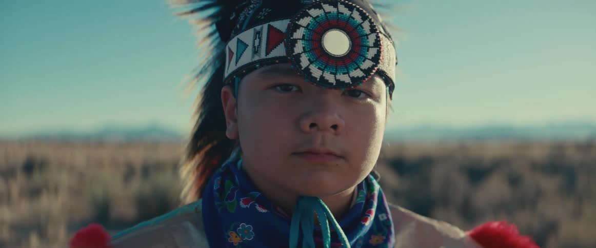 Portrait of a young teenage boy wearing native american attire while standing in a natural setting during the day