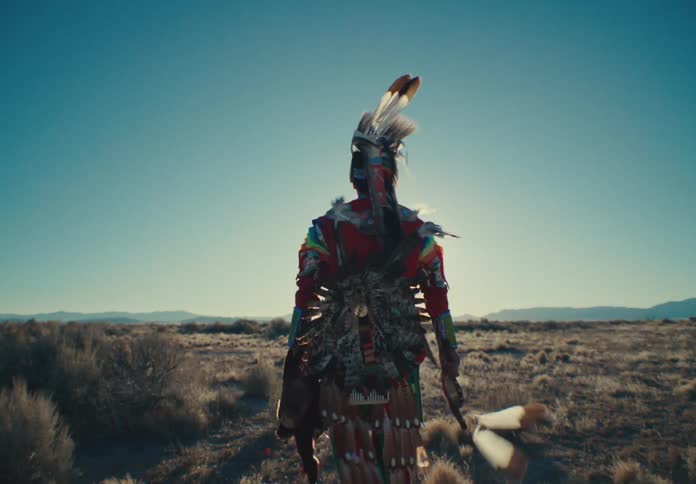 Person in native american attire walking through natural environment with the sun on the horizon