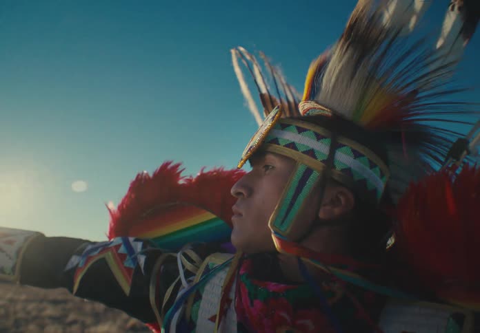 Man wearing native american attire poses during a performance outdoors on a windy day