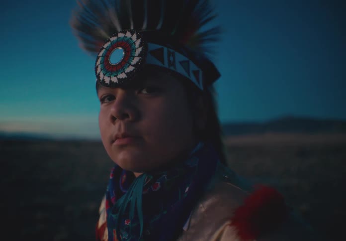 Portrait of a young native american man wearing traditional dress while standing in a field on a morning