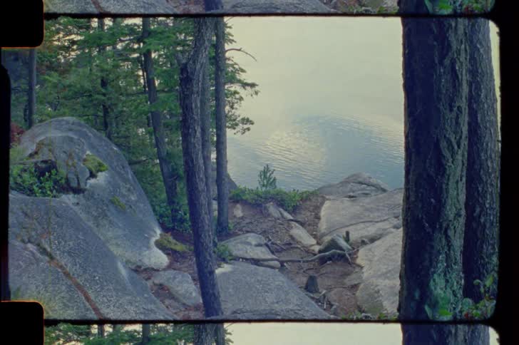 A rocky cliffside overlooking a calm reflective lake surrounded by trees