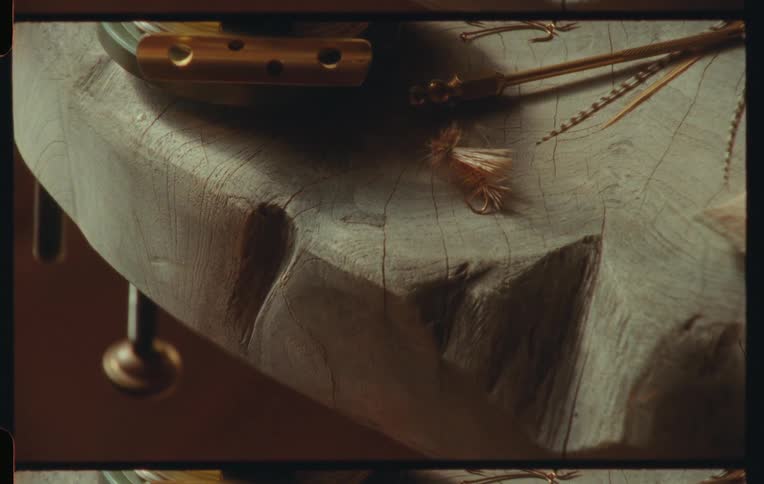 Close up of fishing gear including a fishing fly and fishing reel on a rustic wooden surface