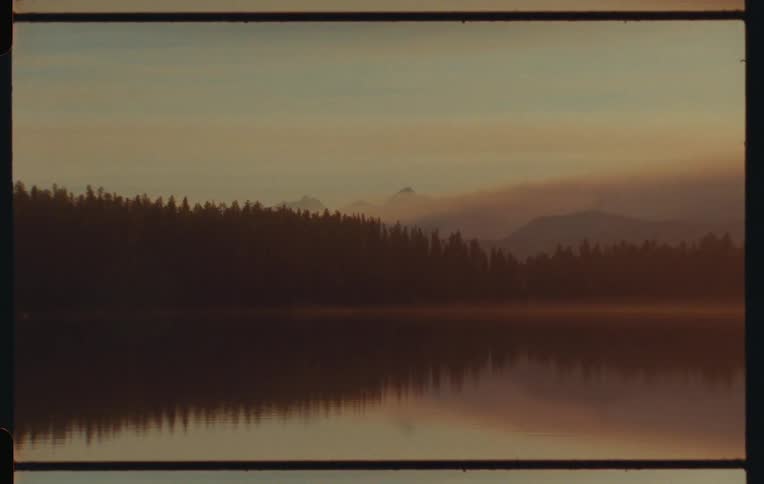 Landscape of a calm lake surrounded by conifers and with the silhouette of mountains in the background