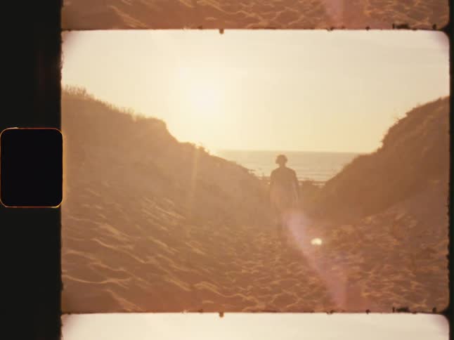 A silhouette of a person walking through a sandy pathway with a golden sunset in the background