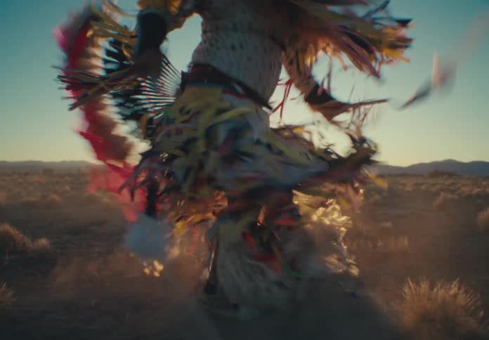 A person in ritualistic feather clothing is performing a dance while spinning in a desert region