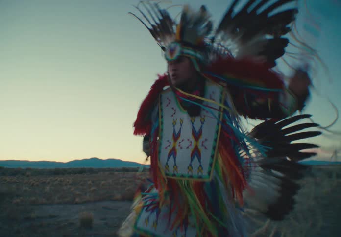 Two native american dancers in elaborate traditional regalia perform a vibrant rhythmic dance in a sun drenched desert landscape