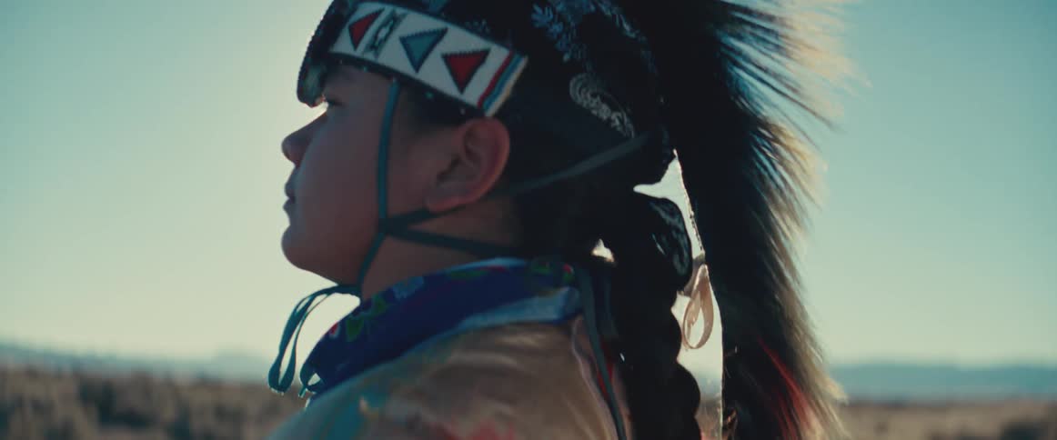 Side portrait of a native american girl wearing traditional attire with a feather on her head