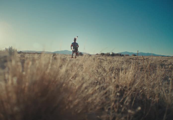 A person in a desert region with beige grass and is doing a ritualistic dance