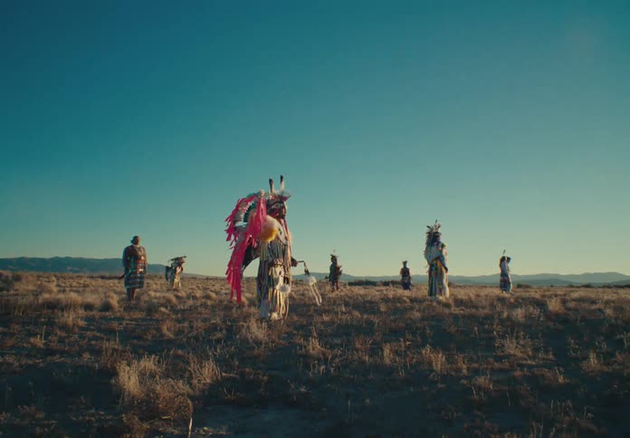 Group of people in traditional native american clothing in a field with scrubland