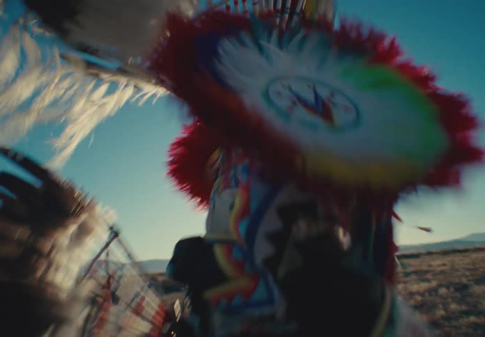 Native american man wearing a costume dancing in a desert field with undergrowth