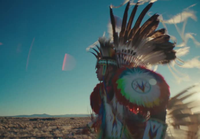Male dancer wearing native american attire dances in a field back lit by the sun