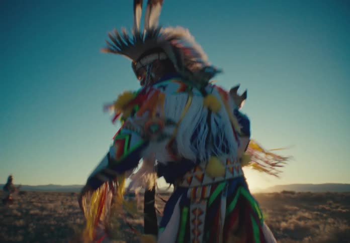 People from a native american tribe dancing in a field with the sun on the horizon