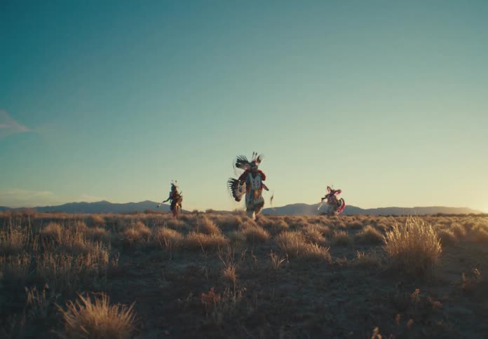 Male dancers wearing native american attire perform a traditional dance in a field during the day