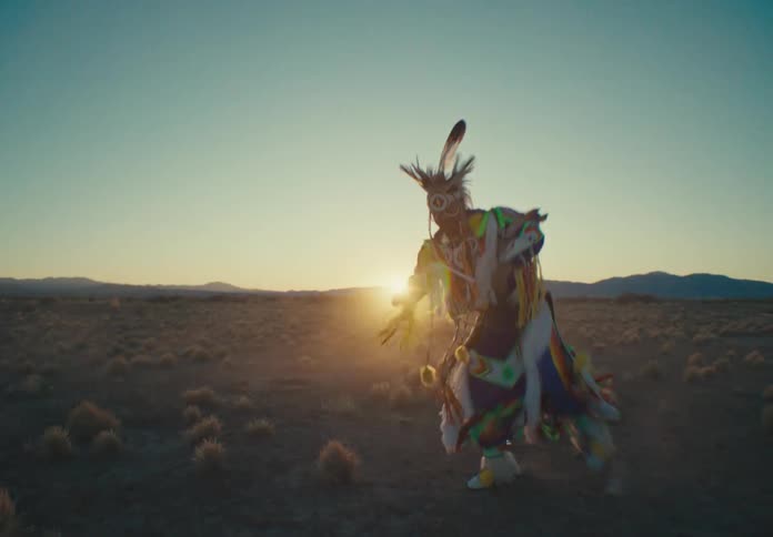 Person in native american attire dancing in a field as the sun sets on the horizon