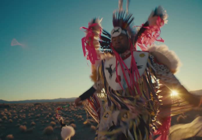 Native american man dancing in ceremonial attire in natural setting with silhouettes of mountains on the horizon