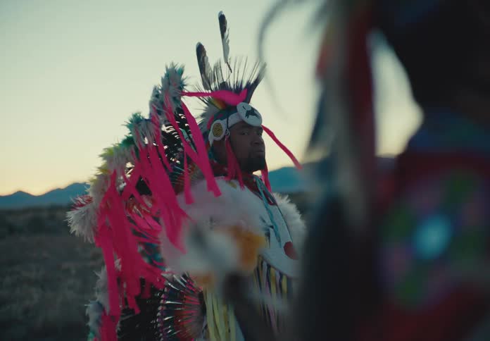 Two people in traditional native american clothing in a natural setting on a morning