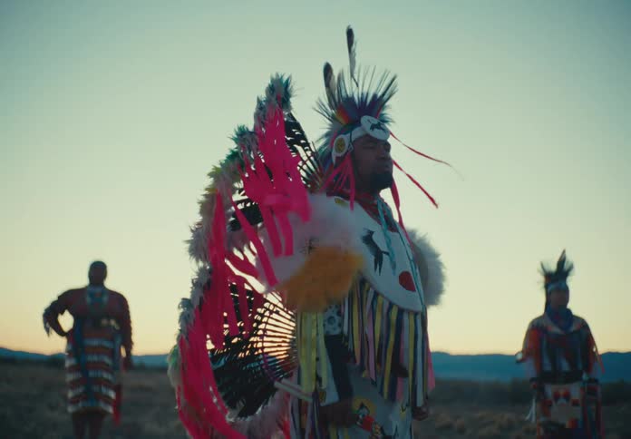 Three people in traditional native american clothing in a natural setting