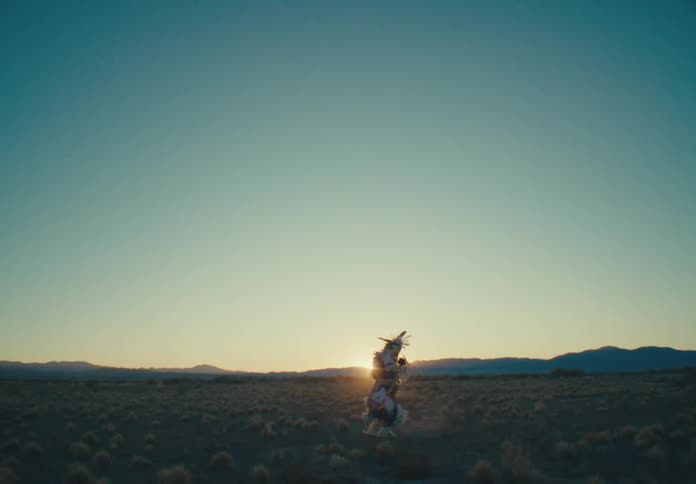 Person in traditional native american attire dancing in a field with the sun on the horizon