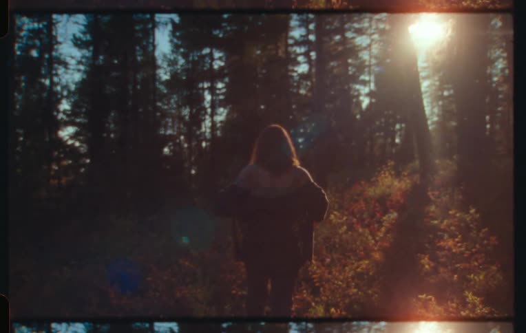 Woman putting on a coat and walking in a forest with sunlight reflection in the late afternoon