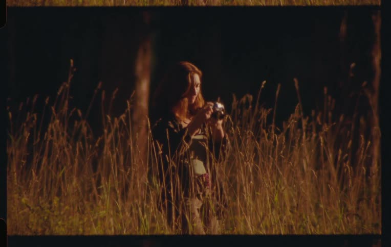 Woman in a field in the late afternoon using a camera