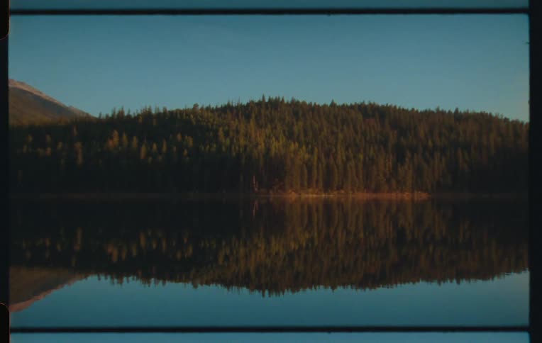 Landscape of a calm lake reflecting the shore with conifers