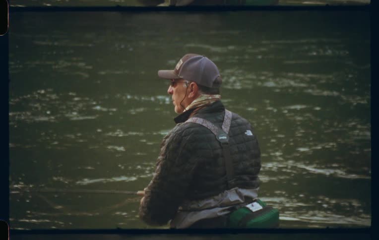A fly fisherman in waders casts his line into a swiftly flowing river