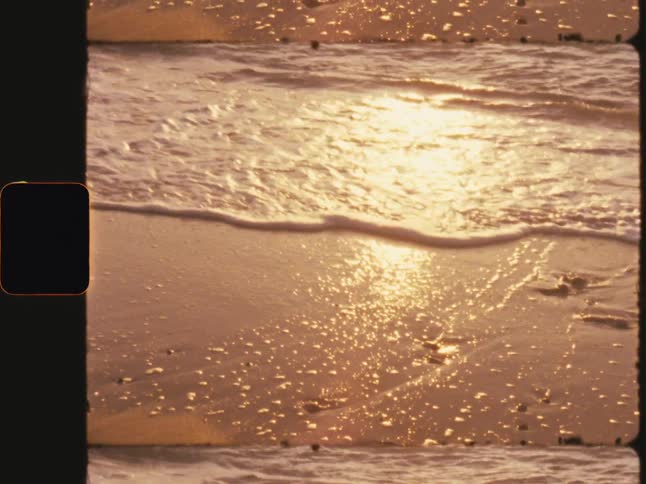 Sea water with foam on the beach sand and the reflection of the sun