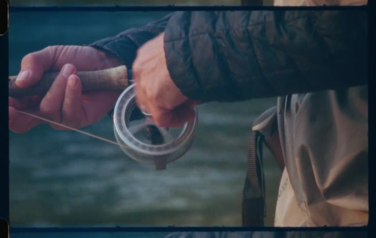 Closeup shot of a fisherman rolling the fishing rod by a river