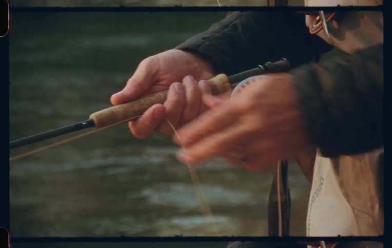 Hands of a fisherman with a rod reeling in the line on the edge of a river