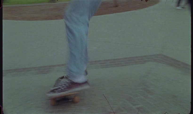 A person is skateboarding on a concrete floor and does a trick with his skateboard on a small ramp