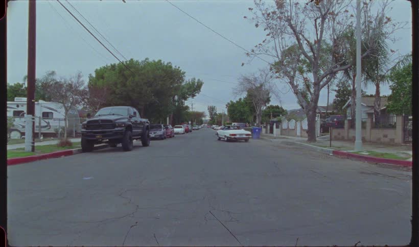 An asphalt street in a residential area with a white car parked on the right side and then it starts driving forward