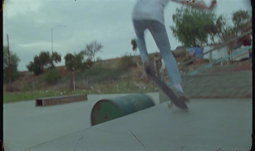 A skateboarder jumps over a metal drum barrel in a park