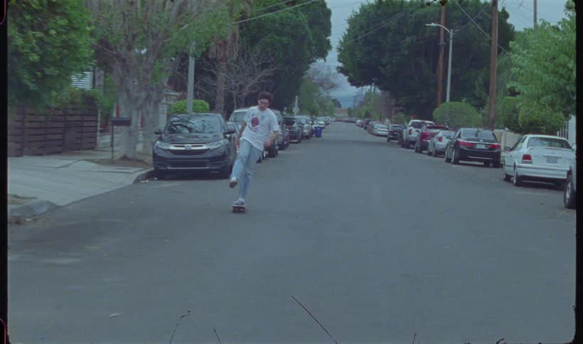 A young man skateboarding down a residential street maneuvering between parked cars
