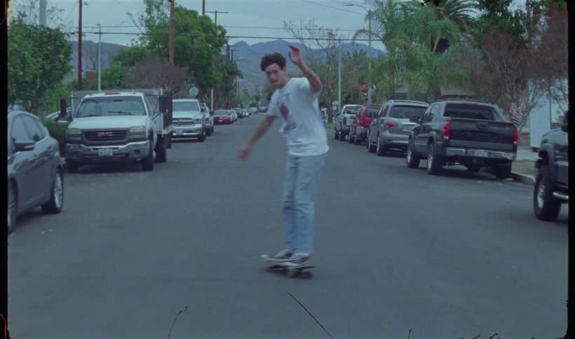 A teenager is riding his skateboard down the road