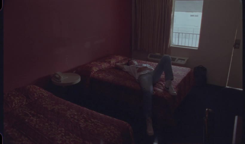 A man reclines on a bed in a hotel room surrounded by soft linens and a serene atmosphere