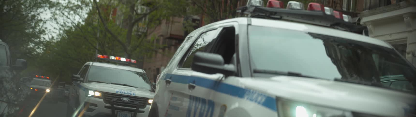 Two police vehicles shine their lights in a city