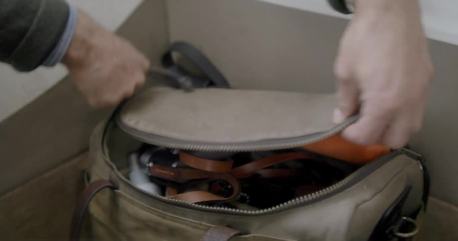 Man unzips a bag to pull out a camera with a strap connected to it