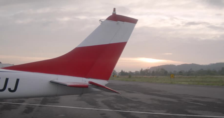 Red and white tail of small aircraft parked on an airfield at sunset