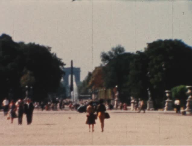 Pedestrians walking through a square with a city and trees around