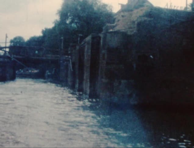 A bridge arches over a canal as a boat glides beneath it with city buildings in the background
