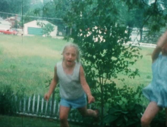 Two blonde girls smile while dancing in their yard on a summer day