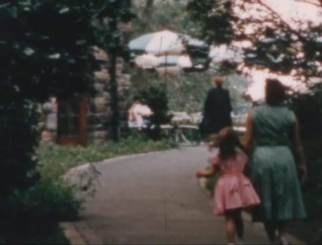 Mother and daughter walking along a path in the park turn to smile behind themselves on a summer day
