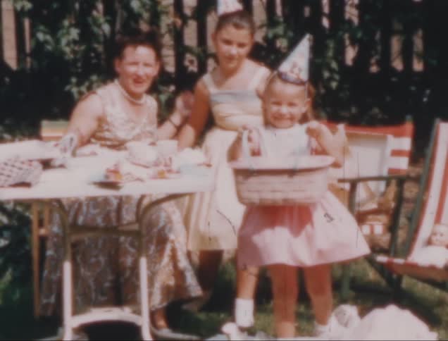 A mother and her daughters are gathered outdoors with the youngest child opening presents at her birthday party