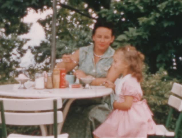 A vintage scene of a woman and a young girl sitting at an outdoor table enjoying a meal or dessert under a leafy tree canopy