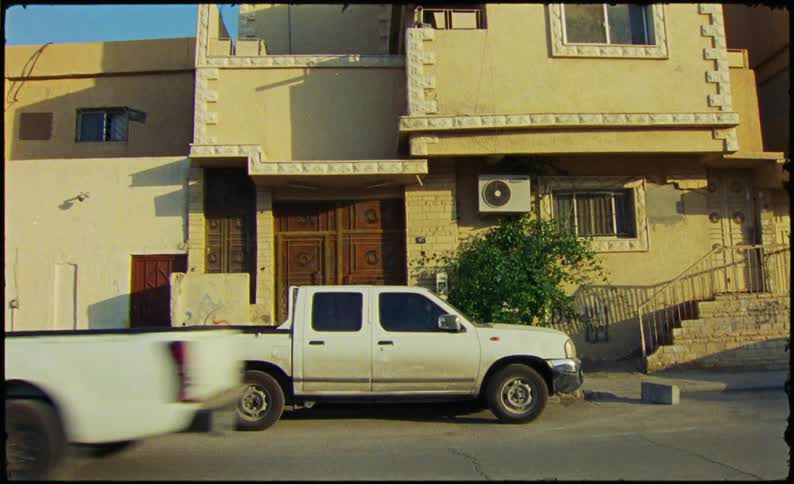 A white pickup truck parked in front of a beige house with a small garden in a neighborhood with other houses visible in the background