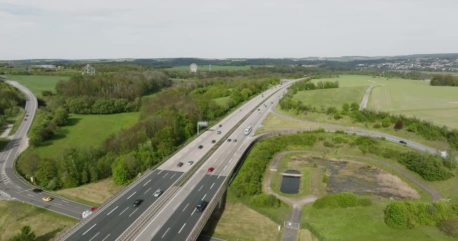 An aerial view of a complex highway interchange with multiple lanes and bridges surrounded by green fields and trees
