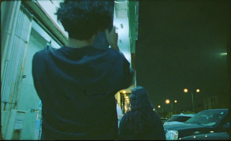 A group of teens walking into a store one swinging a skateboard on their back